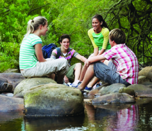 Teenagers Sitting On Stones By River In Forest